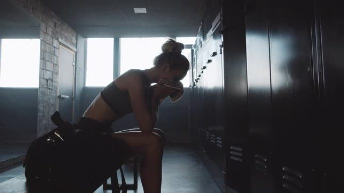 悲伤的欧洲运动女子独自坐在黑暗的健身房更衣室里，在糟糕的一天慢动作后感到沮丧和疲倦。
