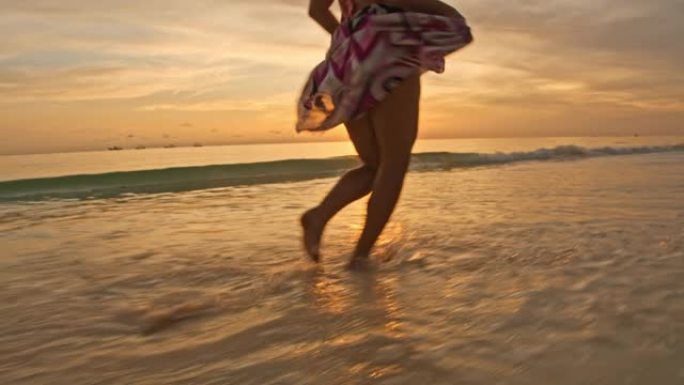 日落时在海滩上奔跑的SLO MO女人
