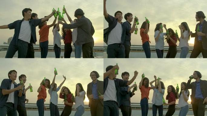 一群年轻的朋友跳舞，玩得开心，在日落背景的夏季屋顶派对上，用烤面包和叮当响的举杯庆祝。慢动作。