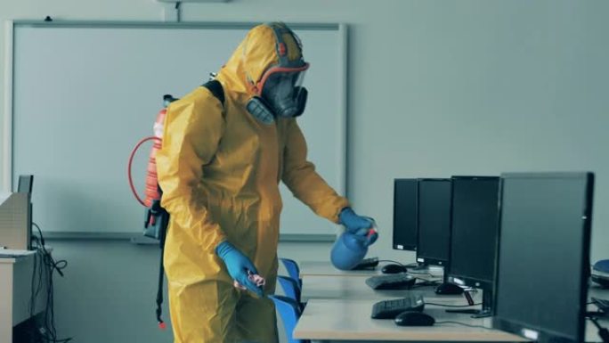 一个穿着危险品套装的男人正在给计算机课消毒