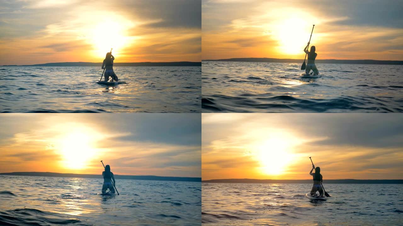 女运动员漂浮在特殊的木板上，在日落背景上划桨。4K。