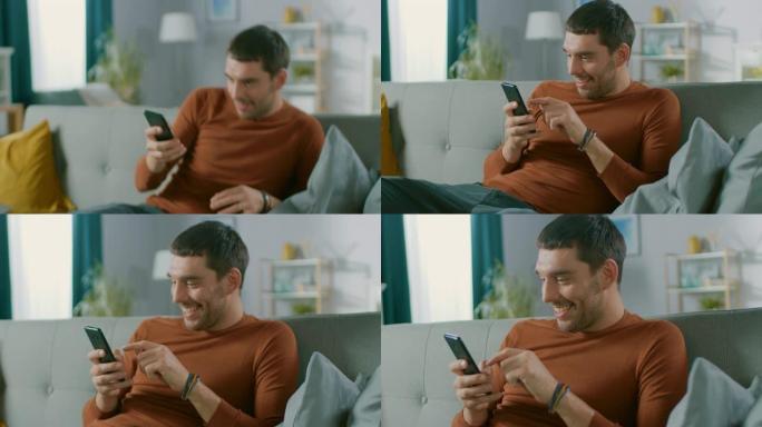 英俊的快乐男人在家里，坐在沙发上，同时使用智能手机，做各种触摸和滑动手势。男人在舒适的客厅里用手机放