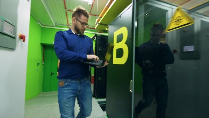 男性程序员在服务器室中行走，用计算机检查机架。