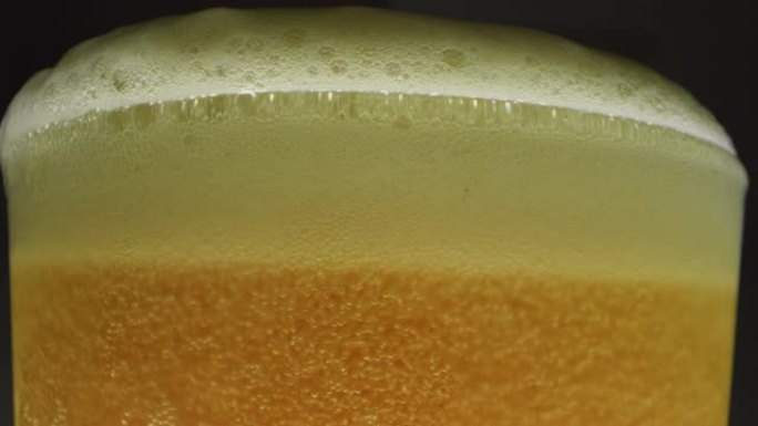 在黑色背景上有一个漂亮的白色泡沫的玻璃杯中关闭一些啤酒。概念: 饮食，宏观。