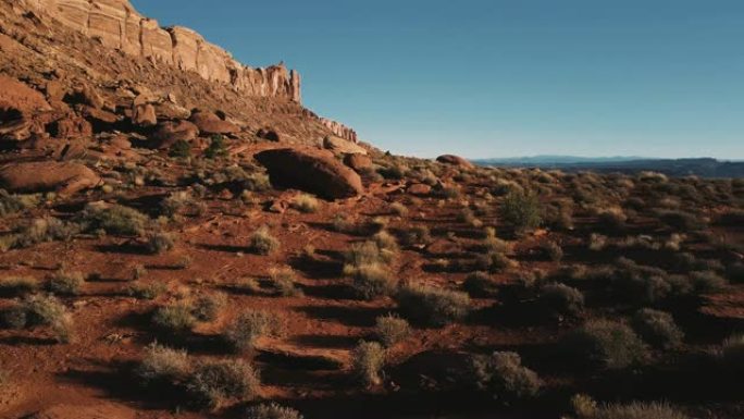 无人驾驶飞机在亚利桑那州巨大的山脉附近低空飞行，砂岩景观覆盖着岩石和阳光明媚的天空。