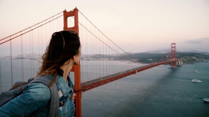 侧景年轻漂亮的旅游女人背包散步看日落风金门大桥的壮丽风景