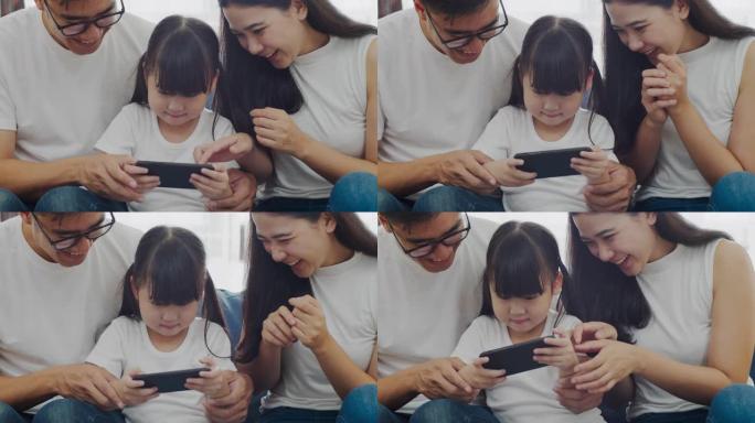慢动作特写镜头: 幸福温暖的家庭父亲，母亲和女儿在智能手机上在线玩有趣的游戏，一起坐在沙发上，父母带