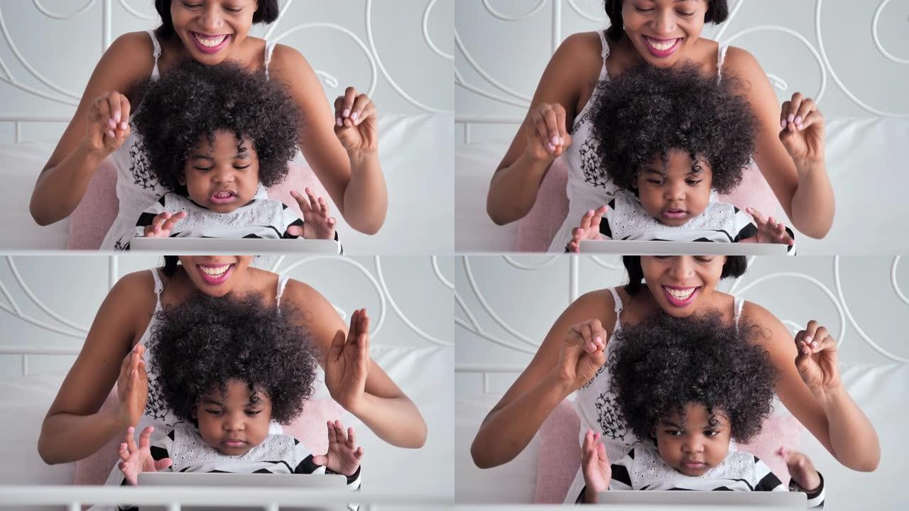 快乐的非洲裔美国母亲和孩子使用笔记本电脑观看，唱歌卡通玩得开心。花时间和她可爱的男婴在家里。家庭，创