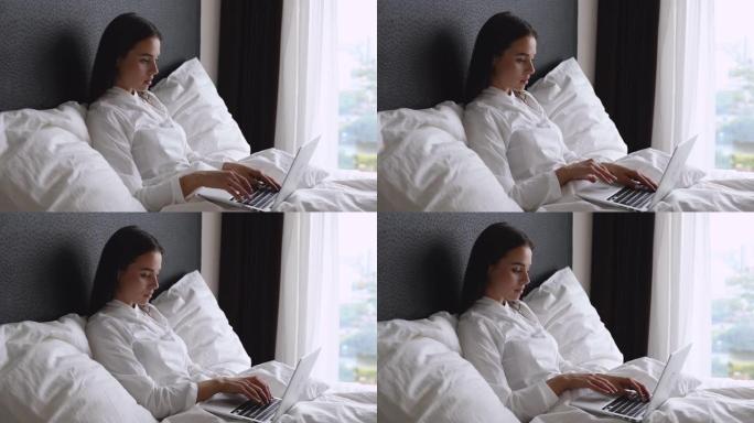 年轻美女早上坐在床上用笔记本电脑