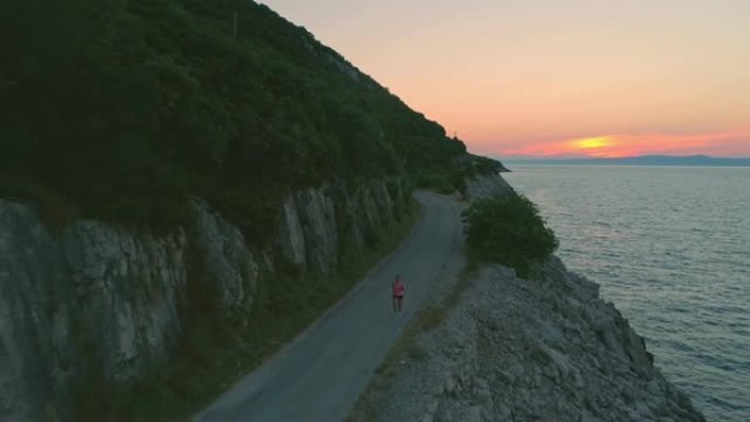 日落时分，空中女子在海边的道路上慢跑