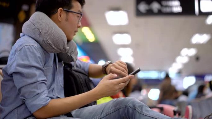 从鞋子平移到在机场等待飞行时使用智能手机的亚洲人的脸