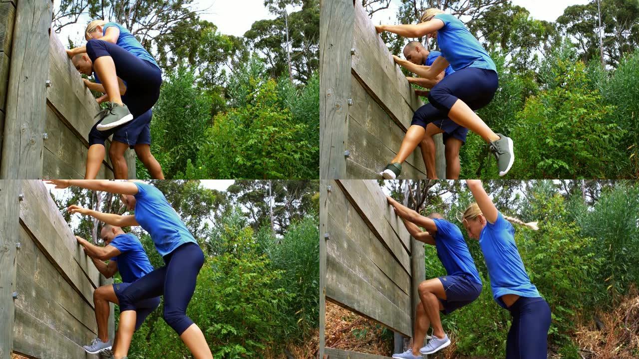 情侣爬升下到一个wooden wall during障碍比赛