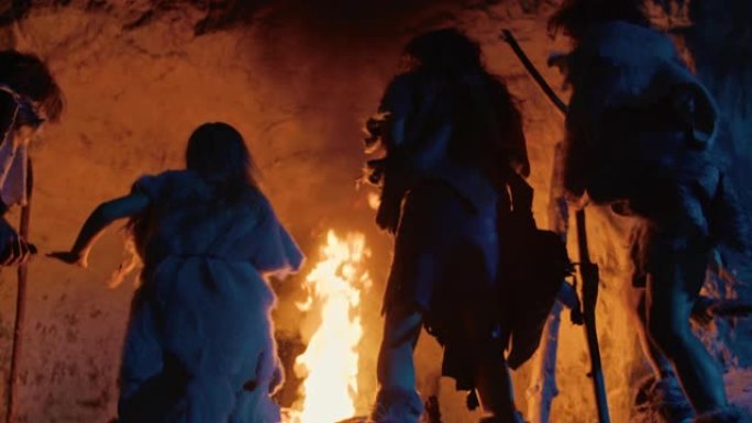 夜间，穿着动物皮的史前狩猎采集者部落在洞穴外的篝火旁跳舞。尼安德特人/智人家庭在火背景慢动作附近做异