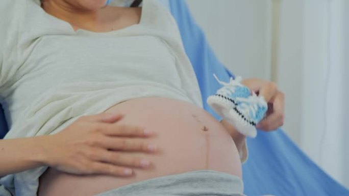 孕妇拿着小婴儿鞋在医院放松。怀孕/分娩