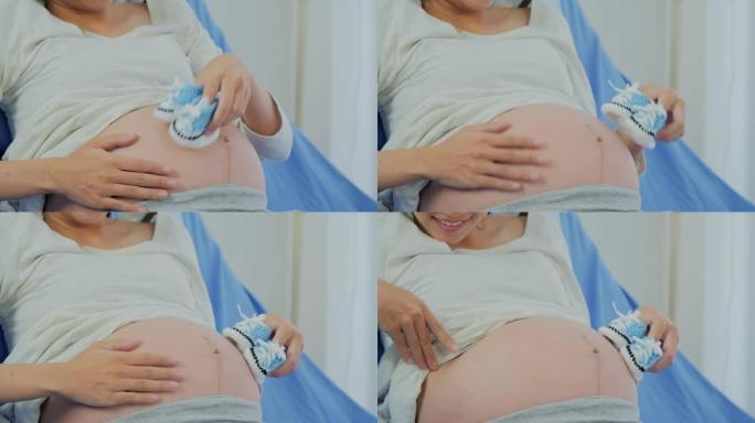 孕妇拿着小婴儿鞋在医院放松。怀孕/分娩
