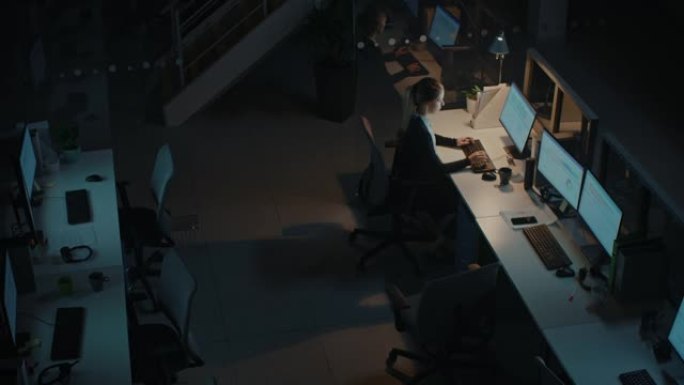 在办公室工作到深夜: 女商人使用台式计算机，进行讨论，分析，使用文档，解决问题，完成项目。高角度放大