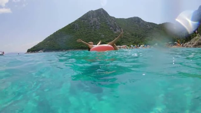无忧无虑的女士在克罗地亚佩列萨克阳光明媚的蓝色海洋上的充气筏上飞溅
