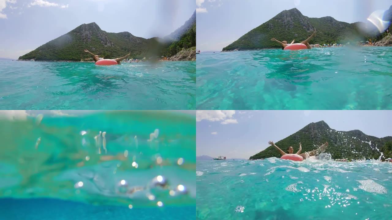 无忧无虑的女士在克罗地亚佩列萨克阳光明媚的蓝色海洋上的充气筏上飞溅