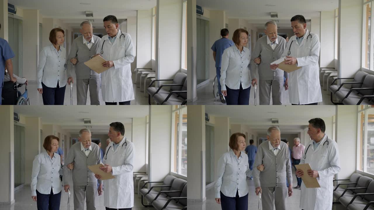 男医生在医院走廊上与高级夫妇交谈时向他们展示了一些考试