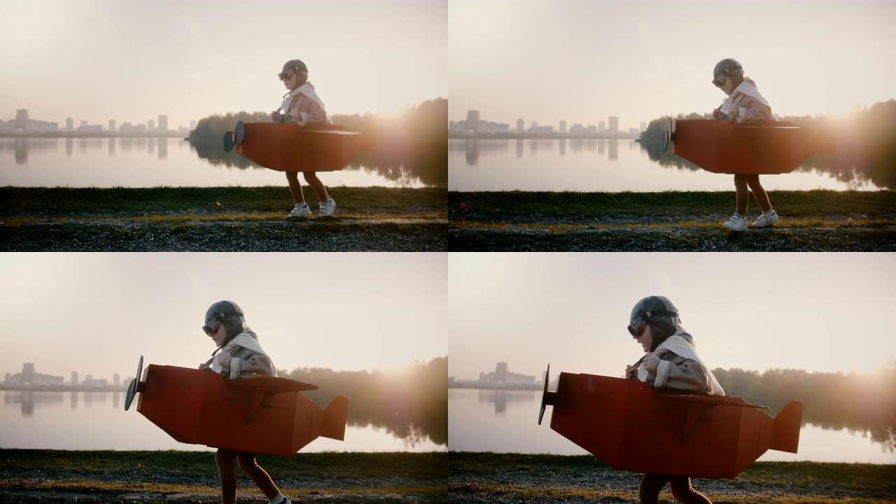 小飞行员男孩开始在日落背光城市河全景的有趣纸板飞机上奔跑，享受着慢动作。
