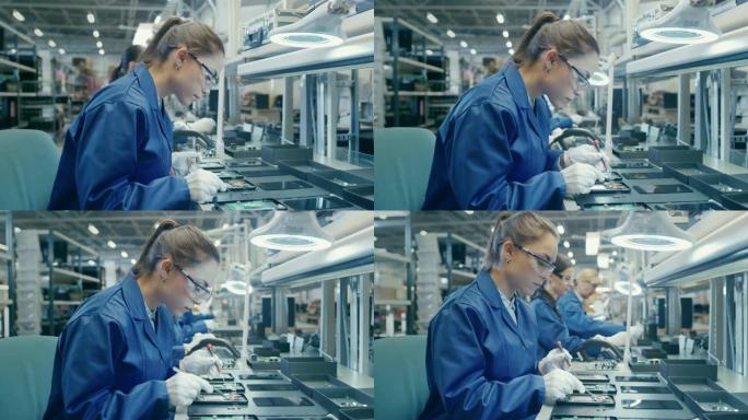 穿着蓝色工作服和防护眼镜的女电子工厂工人正在组装带有镊子和螺丝刀的智能手机。高科技工厂设施，后台有更