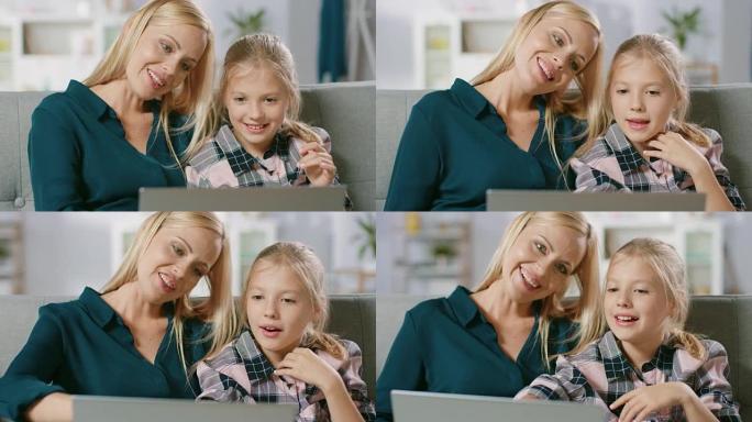 美丽的年轻妈妈和她可爱的小女儿坐在家里的沙发上使用笔记本电脑。一家人花时间在电脑上一起看视频和卡通。