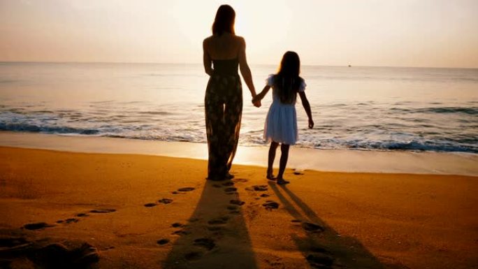 年轻快乐的母女俩一起在金海海滩上走向迷人的日落的美丽背景照。