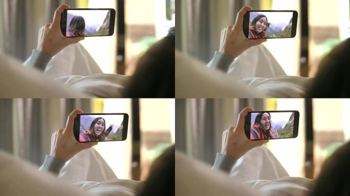 年轻女子拿着智能手机网络摄像头与躺在家里床上的朋友聊天