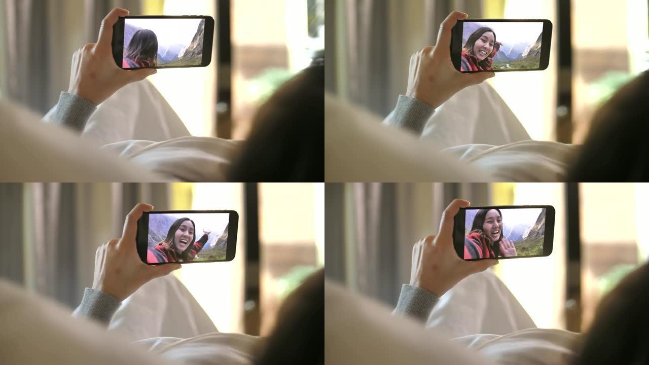 年轻女子拿着智能手机网络摄像头与躺在家里床上的朋友聊天