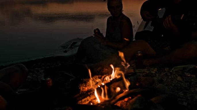SLO MO年轻人在湖边的篝火旁唱歌和弹吉他