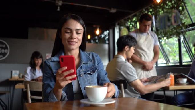 拉丁美洲的女性顾客在咖啡店里一边喝茶一边用智能手机发短信