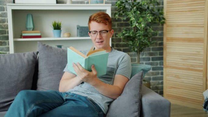 戴着眼镜的帅哥看书，微笑着坐在公寓的沙发上