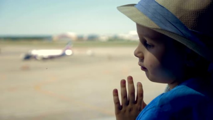 靠近窗户的小男孩，关闭。一个男孩透过大窗户看着跑道上的飞机。