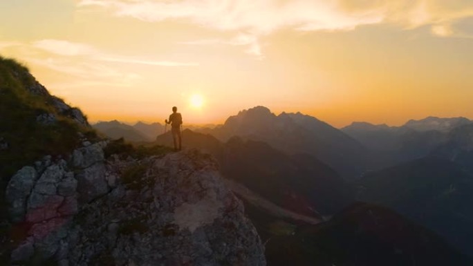 镜头耀斑: 令人惊叹的日落照亮了站在悬崖上的阿尔卑斯山和徒步旅行者。
