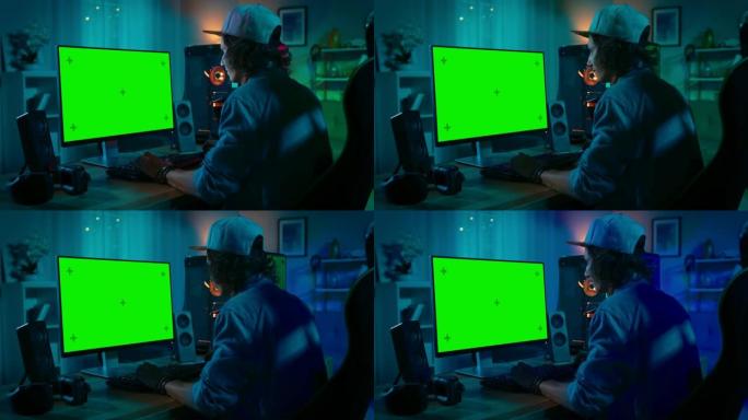 专业玩家在他功能强大的个人电脑上玩在线视频游戏，配有彩色霓虹灯发光二极管灯。绿屏模型。年轻人戴着帽子