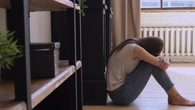 沮丧悲伤的女孩坐在地板上独自在家哭泣