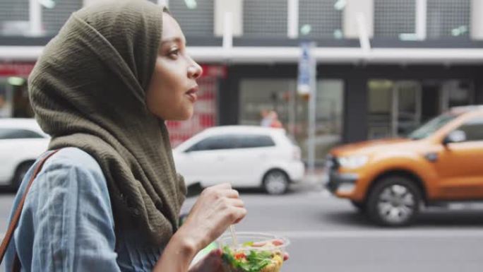戴着头巾的女人在街上散步吃外卖沙拉