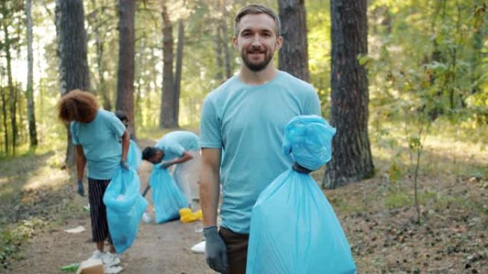 志愿者团队成员在森林里拿着垃圾袋，对着镜头微笑