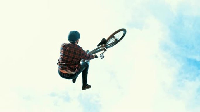 年轻男子女士在多云的天空中跳跃，旋转BMX自行车