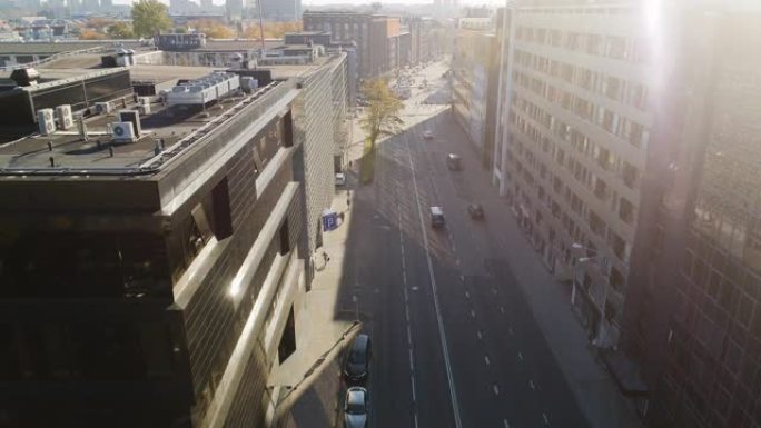 空中无人机镜头在轻车交通的城市街道上方飞行。晴天在两排办公楼之间的街道上。