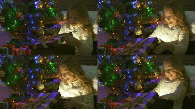 小女孩在圣诞树附近打开礼品盒