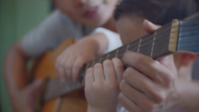 父亲在家教儿子在客厅弹吉他，特写