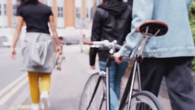 用滑板和自行车穿过城市街道的女性朋友的后视图
