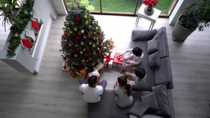 带着两个孩子的家庭走进客厅，在圣诞节早晨打开树上的所有圣诞节礼物