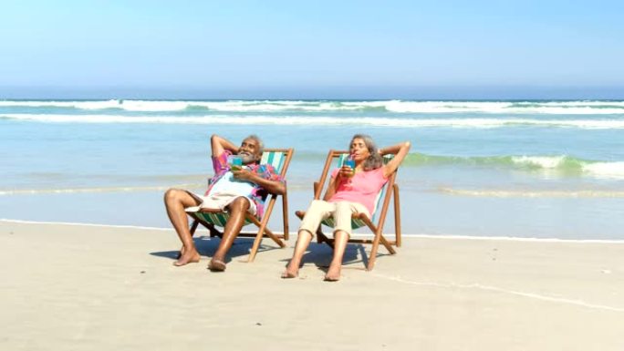 活跃的老年非洲裔美国夫妇在4k海滩躺椅上喝酒的前视图