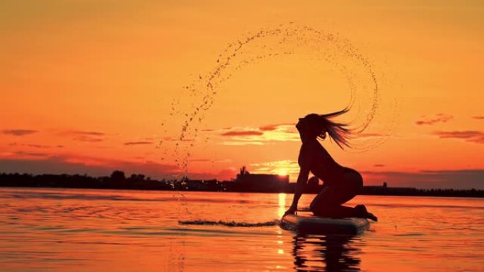 冲浪板上女人翻转湿头发的超级SLO MO剪影