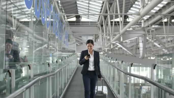 女商人走在机场航站楼，使用智能手机。