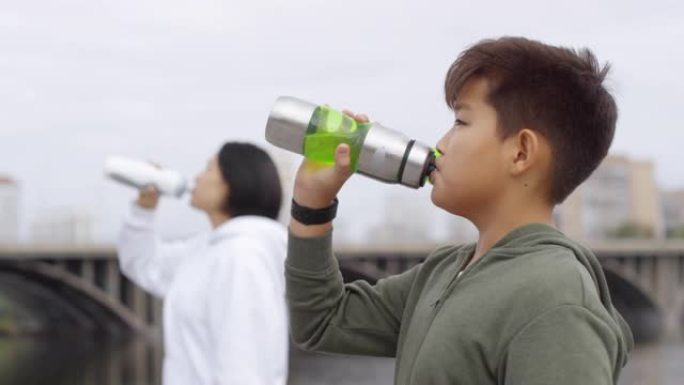 亚洲男孩与母亲跑步后喝水