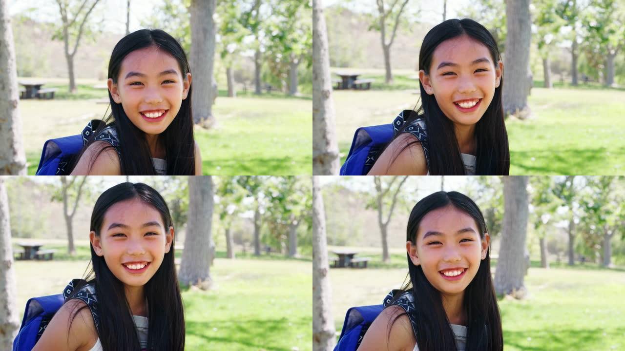 公园里背着背包的年轻女孩的慢动作肖像对着镜头微笑