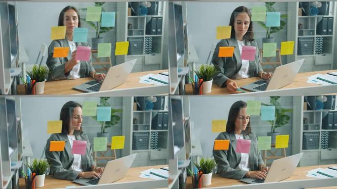 在办公室工作的年轻女子在玻璃板后面用笔记本电脑盖着贴纸